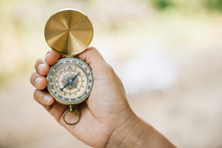 Close-up of a woman's hand holding a compass while hiking in the forest. The compass symbolizes