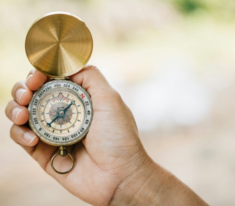 Close-up of a woman's hand holding a compass while hiking in the forest. The compass symbolizes